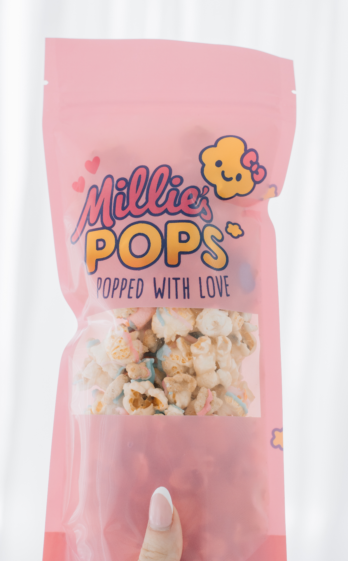 Hand holding Millie's Pops bag with Lucky Charms popcorn